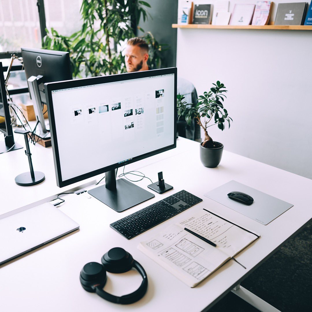 A desk with a computer monitor, keyboard, and notebook